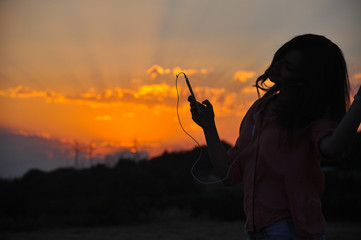 Silhouette of Young Attractive Hipster Girl Listening Music On The Mobile Phone And Dance At Sunset