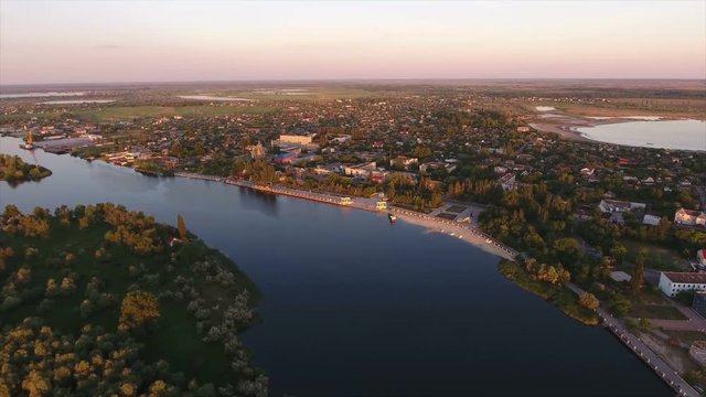 Astonishing view on the curvy Dnipro river  with high trees, summer cottages, and green wetland at a picturesque sunset from a bird`s eye perspective. The skyscape with beaming rays looks gorgeous.