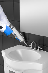 Silicone sealant tube with silicone gun fills the joint between sink and ceramic tiles in bathroom 