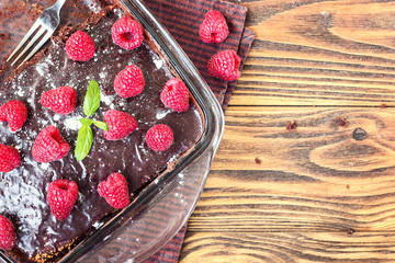 Homemade traditional sweet delicious dark chocolate brownies pie tart cake with chocolate glaze raspberries fruit green mint leaves rustic wooden table background top view baked in glass jar close up 
