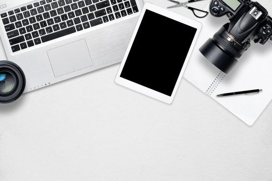 White office photography desk table with laptop, tablet, camera and glass. Top view with copy space