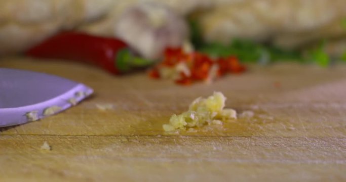 Chef uses flat blade to gather garlic paste from wooden kitchen board. Slow motion