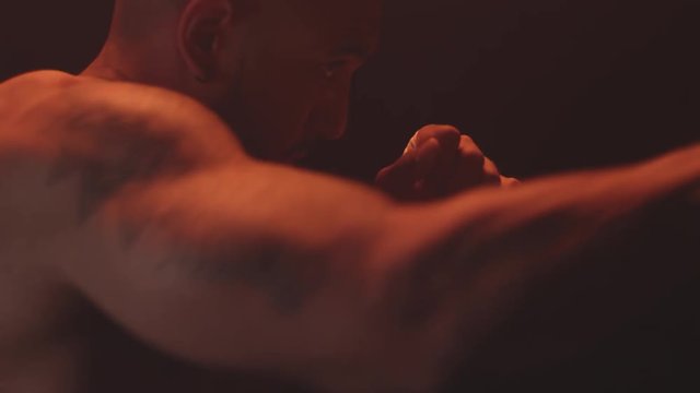 Profile shot of a muscular black man shadow boxing on a foggy dark red background 