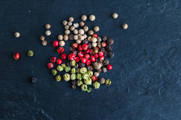 Different types of peppercorns - black, white, pink and green pepe verde - on slate. Top view. Copy...