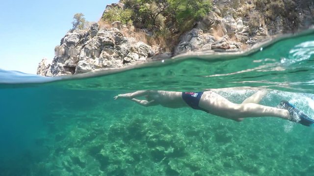 Half underwater close up, swimmer in flippers dives into the sea, raw, 4K