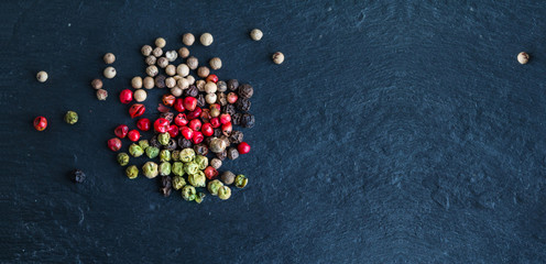 Different types of peppercorns - black, white, pink and green pepe verde - on slate. Top view. Copy space. Wide panoramic image.