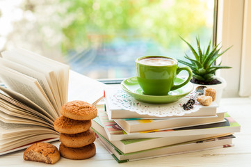Coffee cup, open book, cookies and flower on window with bokeh. Reading and breakfast. Concept warm and cozy home decor - obrazy, fototapety, plakaty