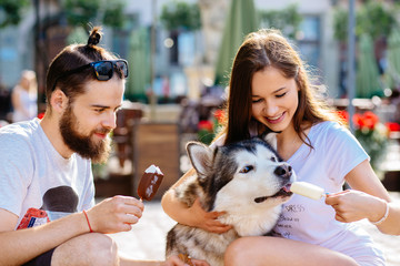Lovely hipster couple feeding ice-cream cute dog on street. Family, pet, animal and people concept.