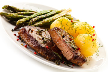 Grilled beef steaks and asparagus on white background 