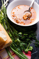 Vegetables and meat in red beetroot soup or borsch in white plate with metal spoon in it on dark marble background.