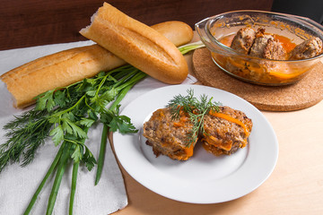 Rissole of pork served on a white plate with white wheat bread and herbs - dill, green onion, parsley around the plate.
