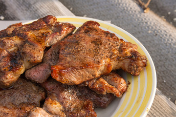 Juicy pork steaks cooked on an open flame grill on big white plate..