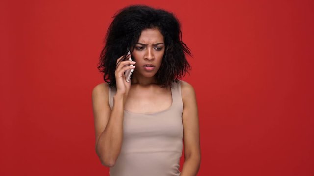 Young angry confused african woman talking by phone over red background