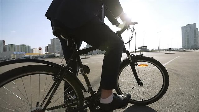 A man in a suit and shoes starts moving on a bicycle in a city in sunny weather.
