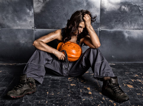 Beautiful tired sexy miner worker in orange helmet with flashlight sitting on a floor on steel background