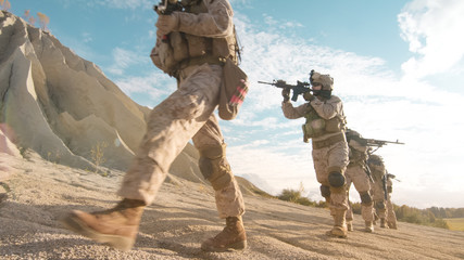 Squad of Fully Equipped and Armed Soldiers Walking in Single File in the Desert.
