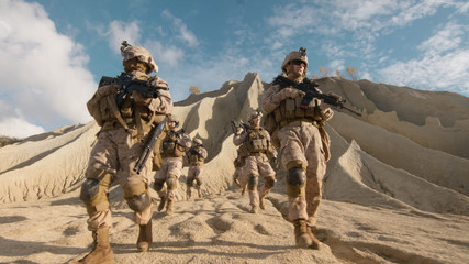 Squad of Fully Equipped and Armed Soldiers Walking down the Hill on the Camera in the Desert.