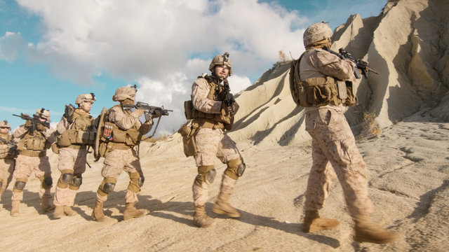Squad of Fully Equipped and Armed Soldiers Walking in Single File in the Desert.