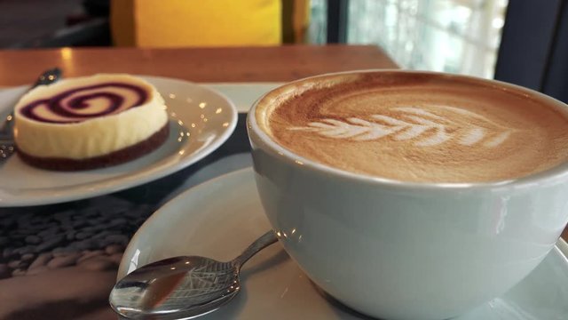 Closeup on a cup of coffee with latte art, a dessert in the blurry background