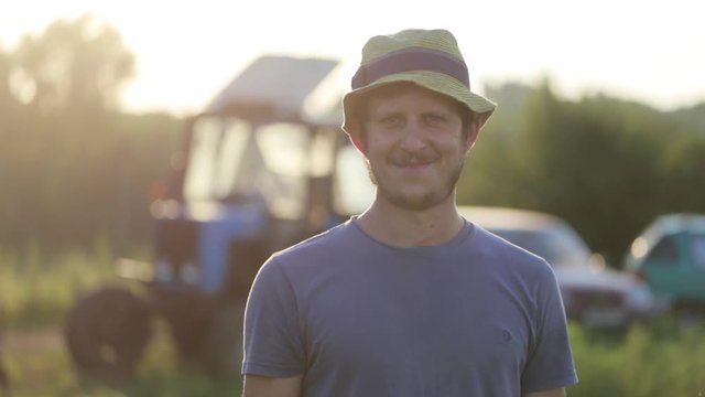 Portrait of young farmer in hat standing at field of organic farm and smiling
