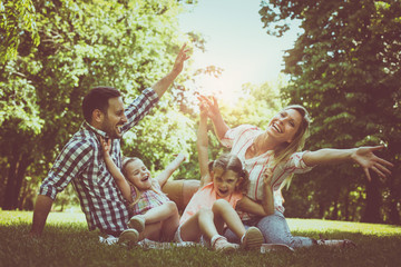 Happy family sitting on grass in the meadow together and enjoying in summer day.