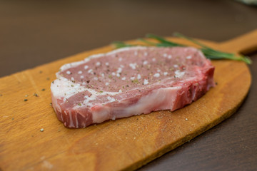 Raw pork steak with salt pepper ans rosemary on wooden board