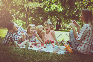 Fototapeta premium Happy family enjoying in picnic together. Family in meadow. Mother taking self-picture.