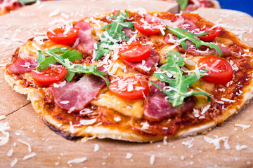 Homemade pizza with prosciutto, tomato, arugula on wooden board blue background