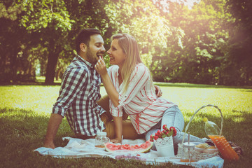 Young happy couple having picnic in the meadow.  Girl gives her boyfriend cherry.