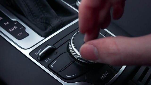 A man turns and presses a knob on the gearshift box of a luxurious car - closeup