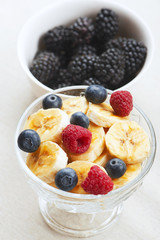 Tasty banana breakfast with raspberry and blueberries next to bowl with blackberries.