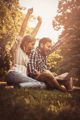 Young couple lying on the grass. Happy couple using laptop.