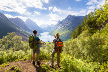 Two hikers at viewpoint  in mountains with lake, sunny summer - obrazy, fototapety, plakaty