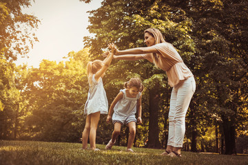 Fototapeta premium Mother with two child in meadow. Mother holding hands with girl other girls passing under the arm