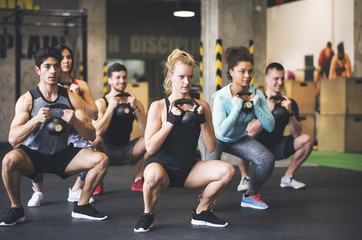 Group of young fit people lifting kettlebells in gym