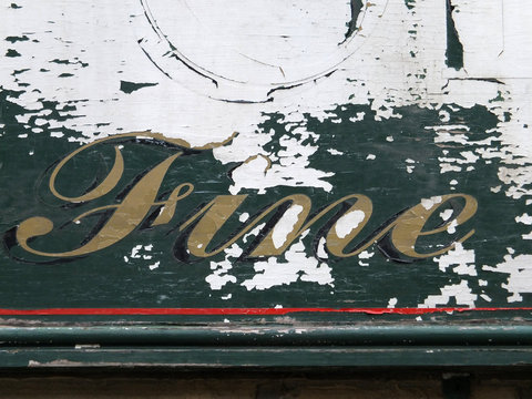 the word fine in hand written script on an old peeling decayed wooden sign