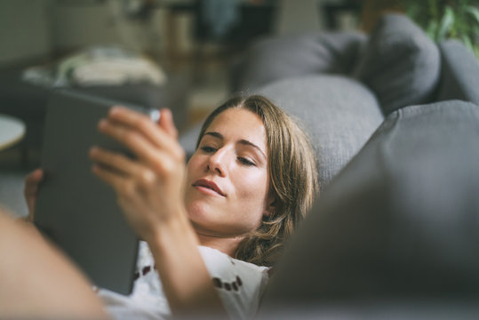 Relaxed young woman lying on couch using tablet