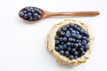 Fresh  blueberries in a cup and a spoon on a white surface of a table. Closeup, top view.