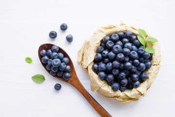 Fresh  blueberries in a cup and a spoon on a white surface of a table. Closeup, top view.