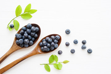 Fresh  blueberries in a wooden spoons on a white surface of a table. Closeup, top view.