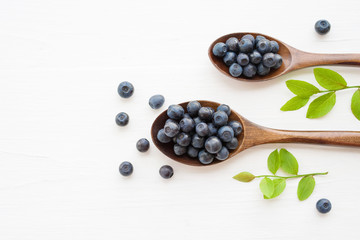 Fresh  blueberries in a wooden spoons on a white surface of a table. Closeup, top view.