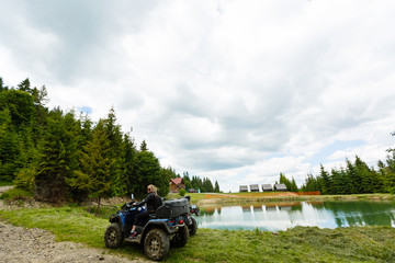 A happy woman riding a quad bike near a lake in the mountains