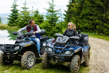 Young couple having fun on mountain while driving a quad bike on a summer day. Young man and woman on an ATV.