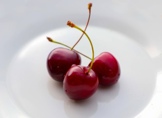 Three cherries berry on a white plate. Cherry ripe delicious fruit on the white background.
