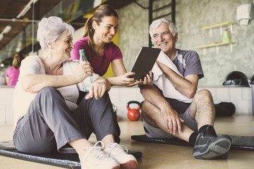 Senior couple in rehabilitation center. Personal trainer showing something on digital tablet. - obrazy, fototapety, plakaty