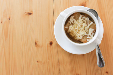 Onion soup on white ceramic bowl with hand on white dish and spoon on wood table texture