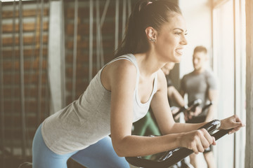 Fototapeta premium People exercise on stationary bikes in fitness class. People workout in gym. Exercise on elliptical machine. Man personal trainer.