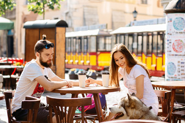 A lovely hipster couple with alaskan malamute dog sitting in street cafe of the city. Family, pet, animal and people concept.