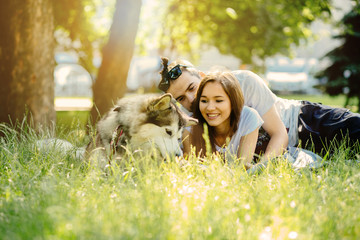 Lovely hipster couple with their alaskan malamute dog lying in the grass in hot summer day. Family, pet, animal and people concept.