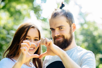 Love is in the air! Beautiful young hipster couple standing close to each other and looking through a heart shape made with their fingers